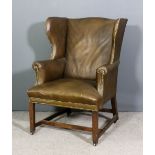 A George III oak framed wing back easy chair, later upholstered in brown leather and studded, on