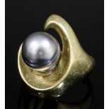 A modern 14k gold mounted black pearl ring, the stylised comma pattern face set with a black