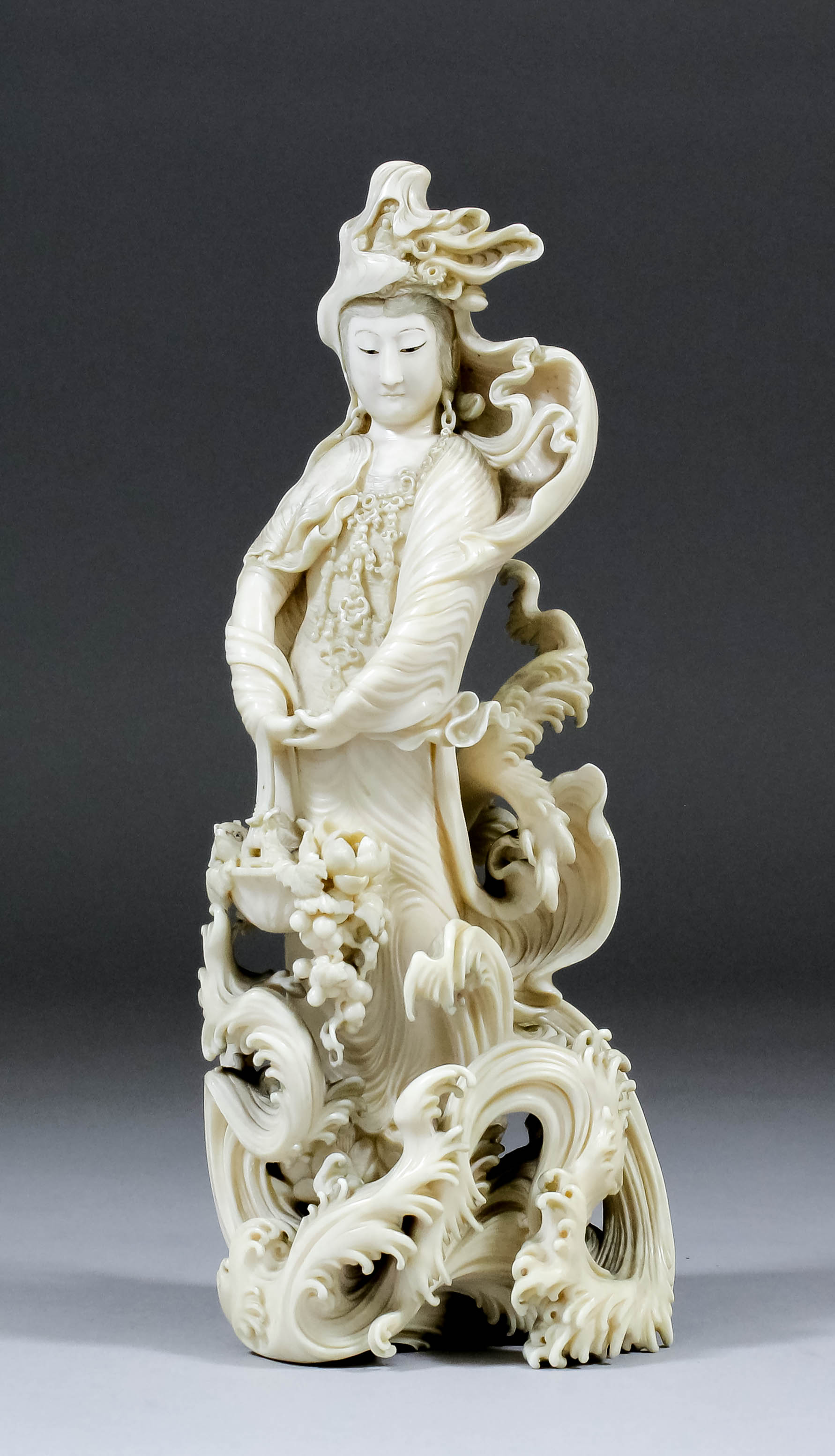 A Japanese carved ivory okimono of a female figure with basket, standing amongst turbulent waves and