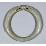 A Chinese pale celadon jade bangle carved with two dragons heads supporting a ball, 3ins (76mm)