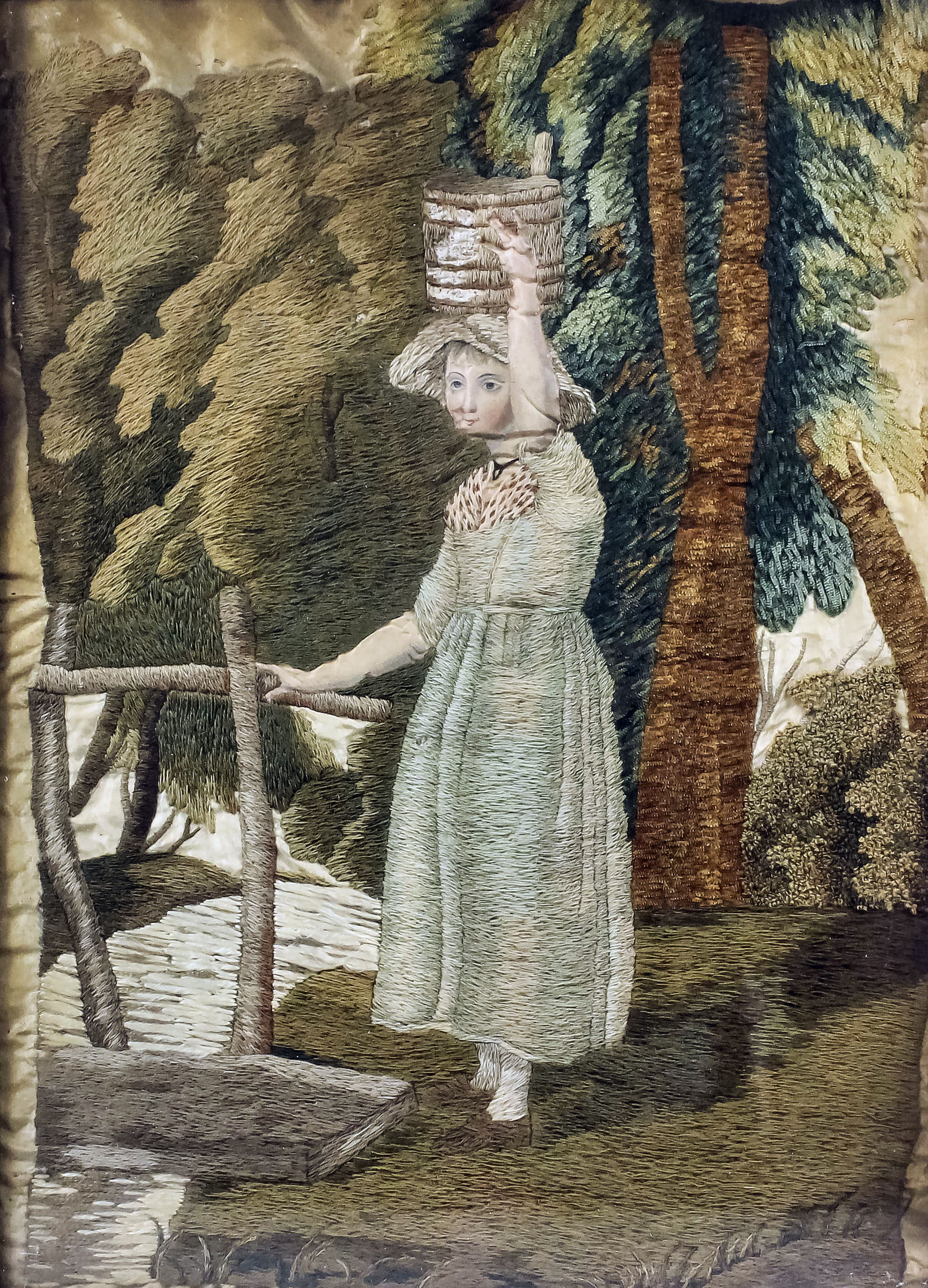 An early 19th Century English coloured silk and woolwork picture of a young girl carrying a basket