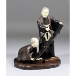 A Japanese carved hardwood and ivory okimono depicting a standing and kneeling scholar studying a