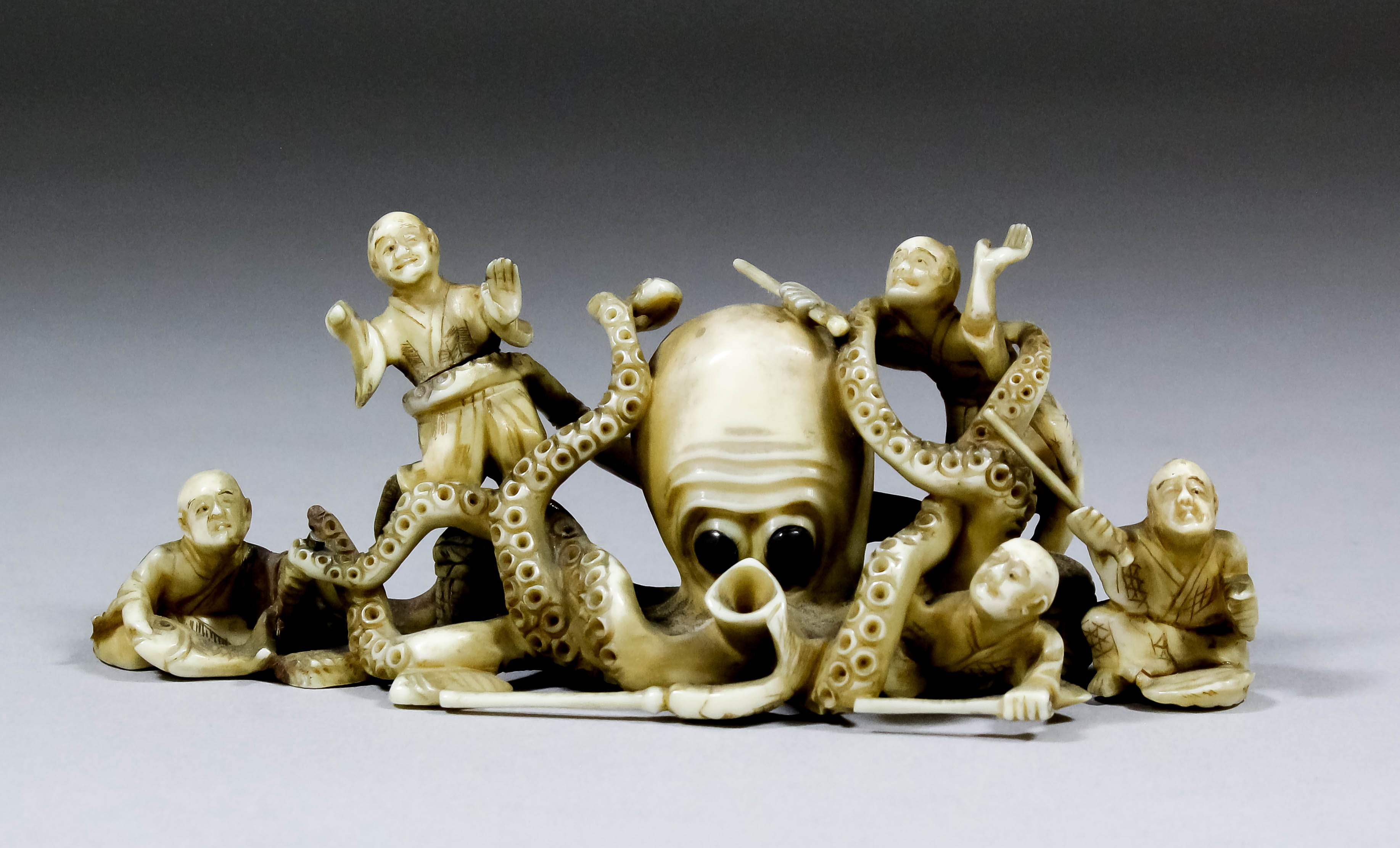 A Japanese carved ivory okimono of five men with sticks being attacked by an octopus, 5ins (127mm)