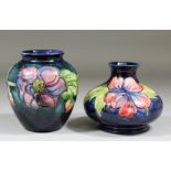 Two Moorcroft pottery vases, both tube lined and decorated in colours with "Orchid" design on a blue