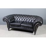 A modern two seat Chesterfield upholstered in black leather, back buttoned, on turned ebonised front