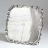 A George V silver square salver of 18th Century design with shaped and moulded rim, on four scroll