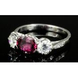 A modern silvery coloured metal mounted ruby and diamond three stone ring, the oval cut ruby