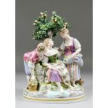 A 20th Century Continental porcelain group of two young ladies in conversation beneath a tree whilst