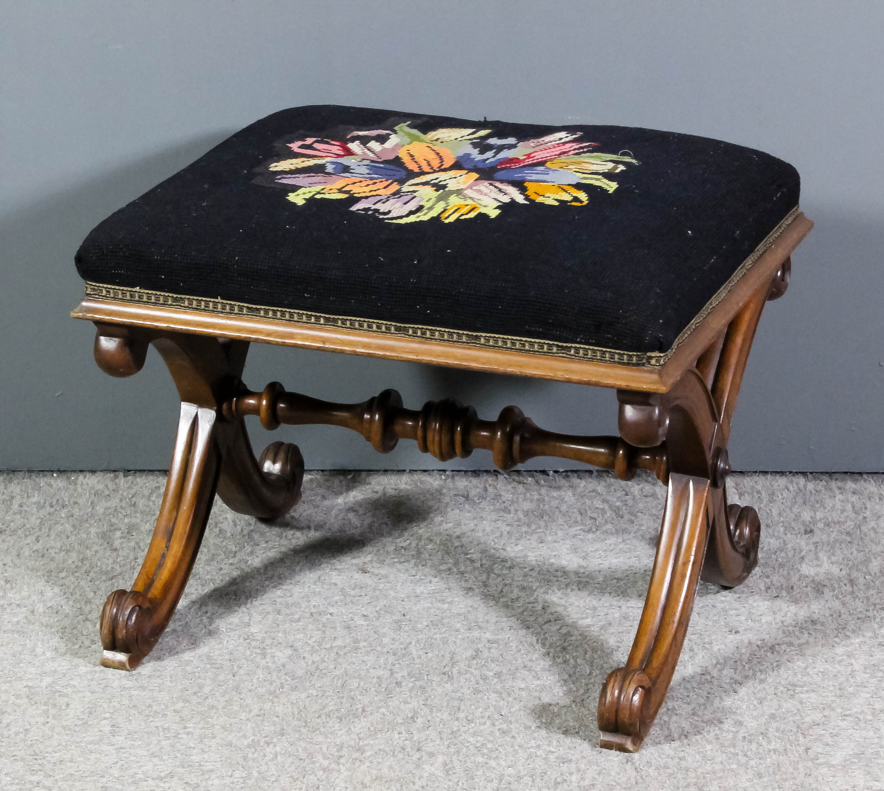 A Victorian walnut framed rectangular stool, the seat upholstered in floral needlework, on moulded