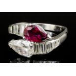 A modern silvery coloured metal mounted ruby and diamond cross-over ring, the pear cut ruby and pear