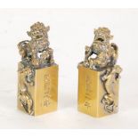 A PAIR OF EARLY 20th CENTURY CHINESE CAST BRASS SEALS, each surmounted by respectively a male and