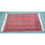 PAKISTAN BOKHARA RUG. With a single row of six guls on a plain crimson field, broad seven striped