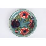 A Moorcroft anemone pattern plate, the purple and pink painted flowers on a turquoise ground, with