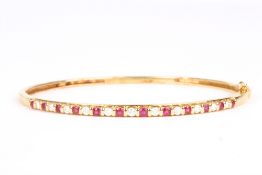 An 18ct gold, diamond and ruby stuff bangle, set with eleven diamonds interspersed by twelve