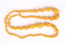 A large graduated amber coloured bead necklace, the beads of uniform honey colour, with two loose