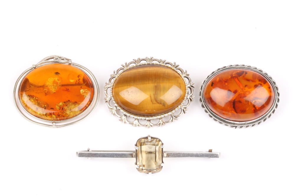 Four silver brooches, one set with tigers eye, two with amber coloured stones, and one with