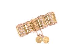 An Eastern knotted gold coloured metal four bar gate bracelet with two coins attached, unmarked,