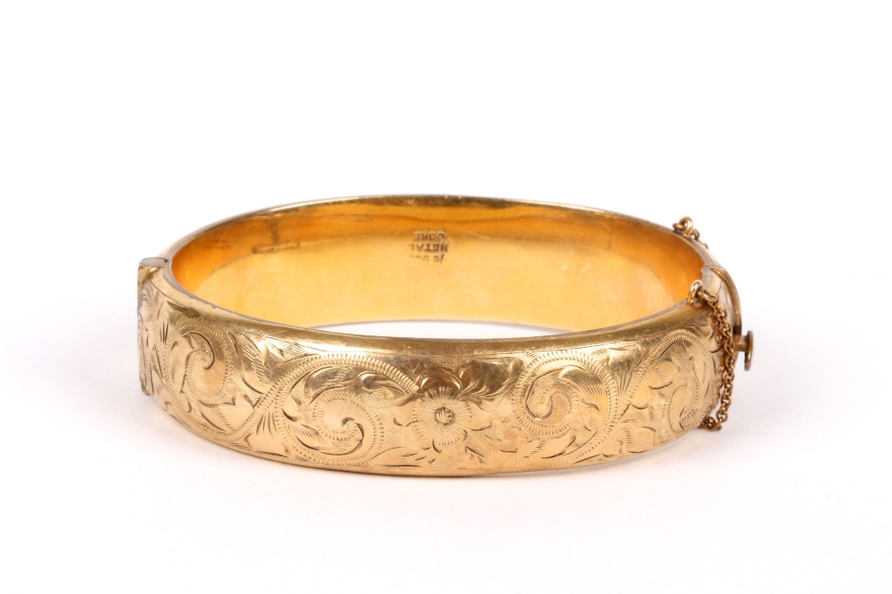 A 9ct gold stiff bangle, with metal core and chased decoration and safety chain .