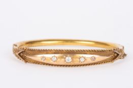 An Edwardian gold coloured metal stiff bangleset with five graduated diamonds in gypsy setting with