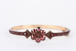 A Bohemian garnet stiff bangle the entire band set with garnets in claw setting on gold coloured