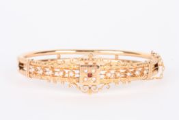 A 19th century style gold coloured metal stiff bangleset with split pearls and garnet in chased and