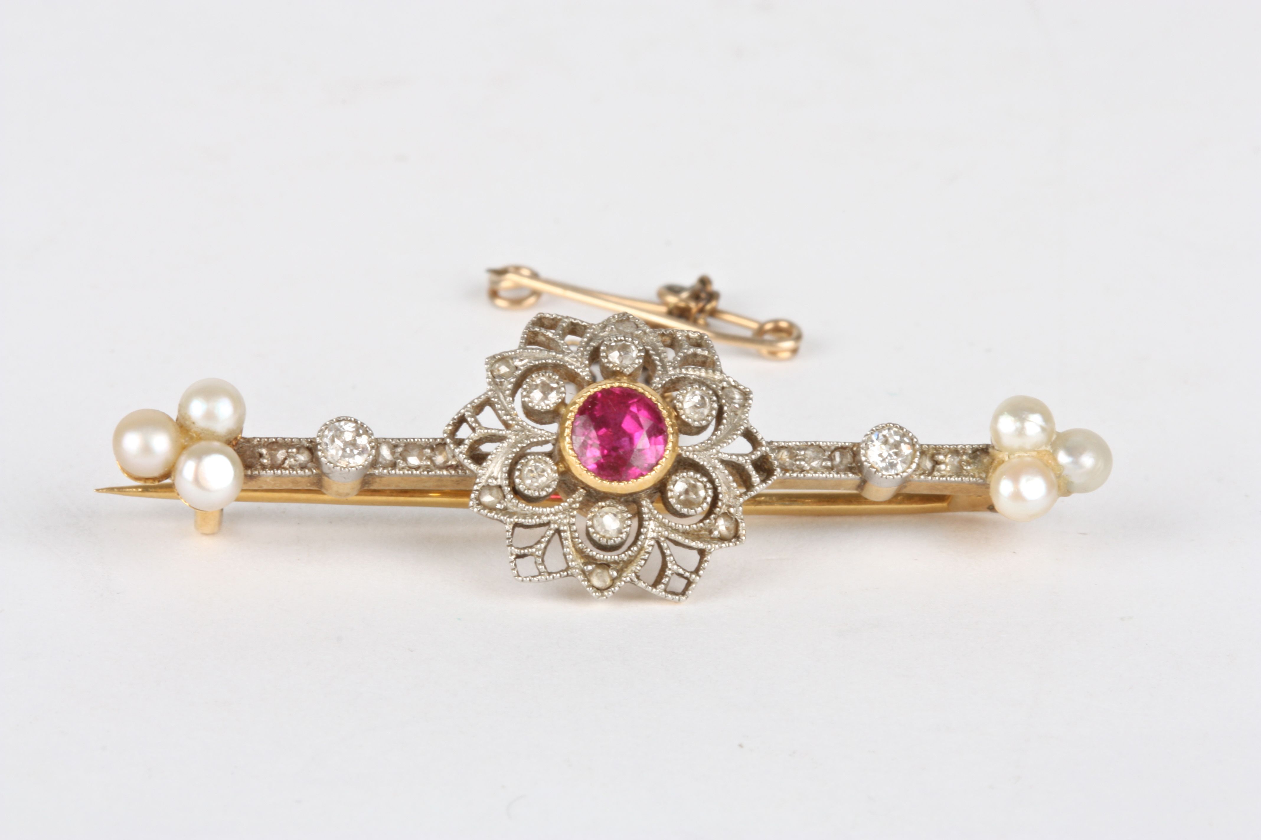 A Victorian diamond, ruby and seed pearl bar brooch
set with a central ruby surrounded by small
