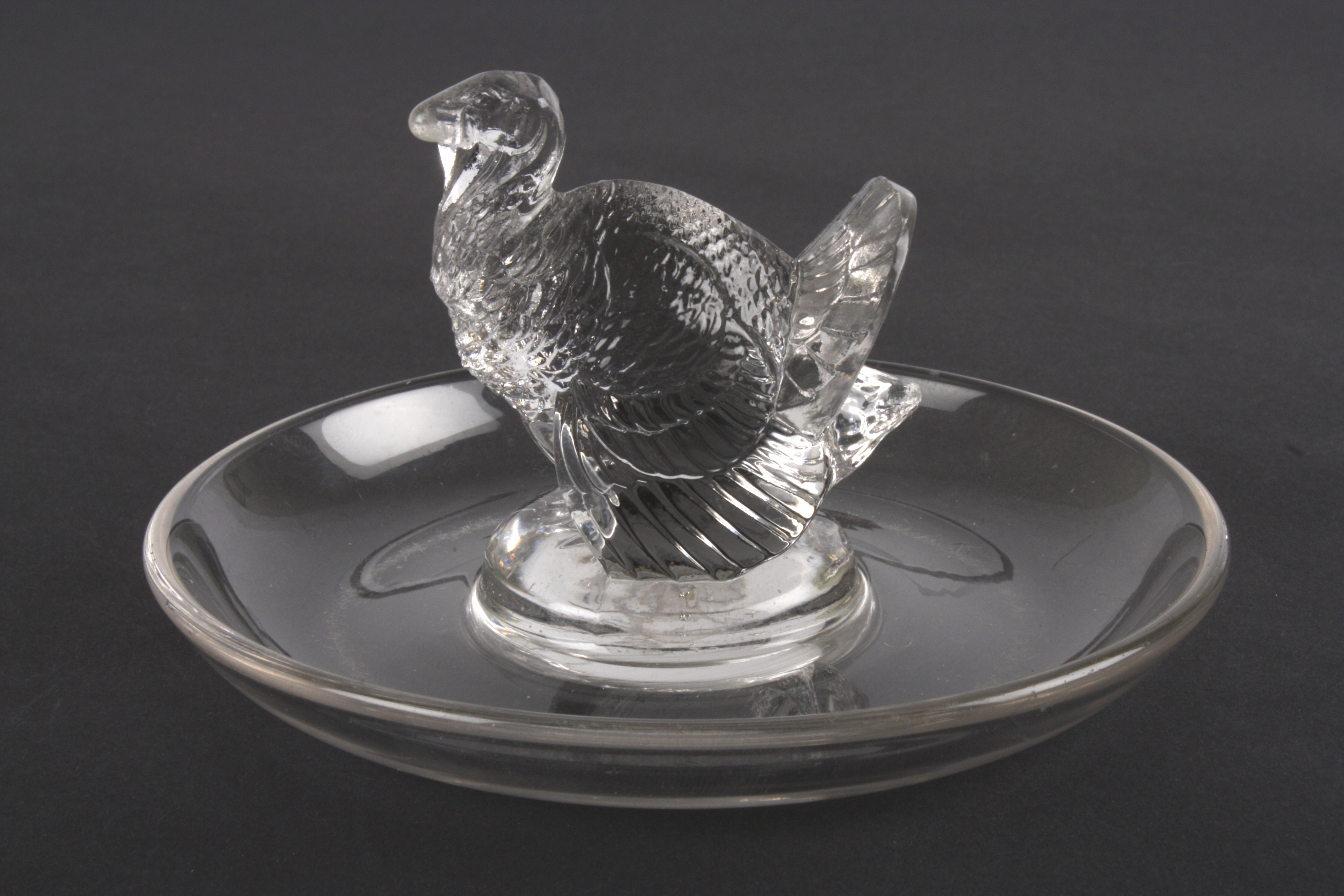 An R. Lalique clear glass ring dish
mounted with a model of a turkey. Etched signature to base 'R.