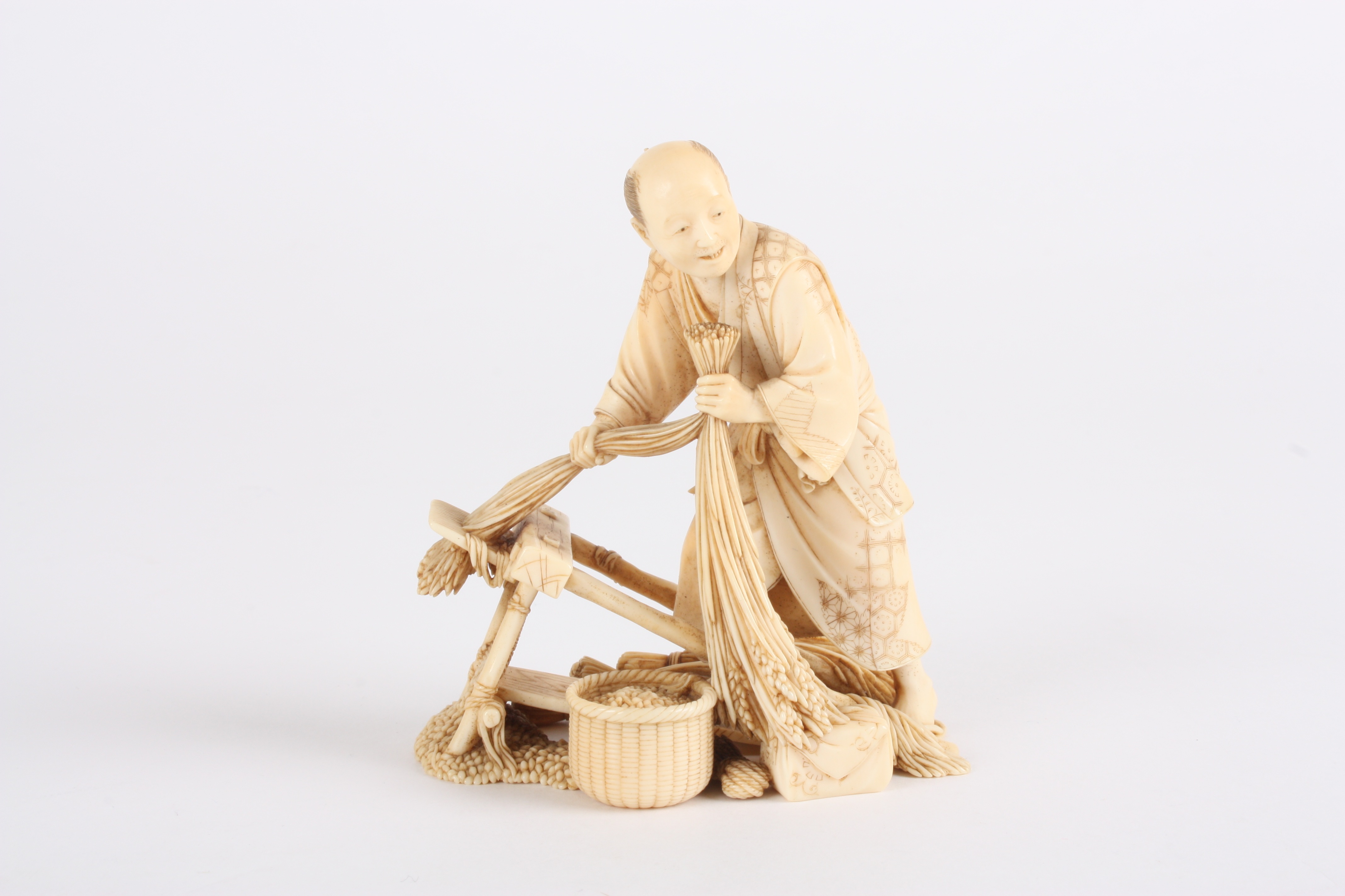 A Japanese finely carved ivory figure of a man
stood threshing corn using a foot operated machine,