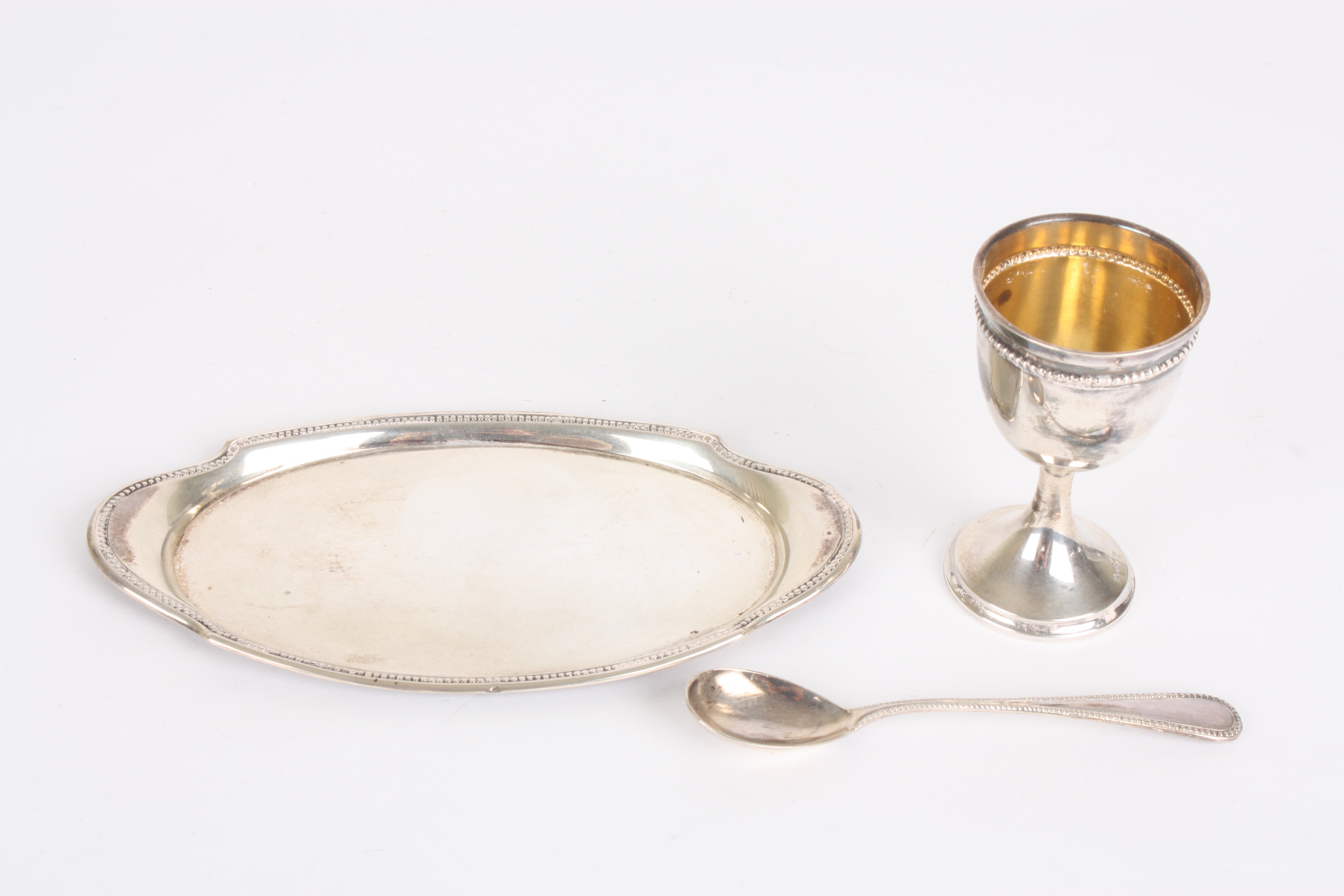 A Continental silver christening egg cup set
comprising an egg cup, spoon and oval tray, with beaded