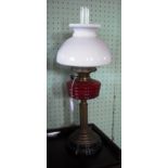 A brass column oil lamp with glass shade and cranberry reservoir.