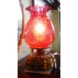 An Edwardian oil lamp, having a brass base and cranberry glass shade, now converted for