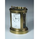 A French oval brass carriage clock with alarm and repeat, shaped handle above rectangular enamel