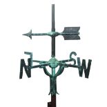 A bronze weather vane, an arrow pointing the direction of the wind above arms lettered for the