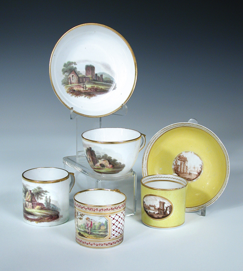 A Coalport trio, a can and saucer and a single can, the first painted with ruins in a landscape, the