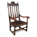 A Carolean oak armchair, with shaped crest rail, turned rail and slat back, scrolling arm