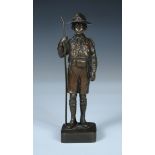 An interbellum bronze figure of a boy scout, the uniformed figure standing on a square base, a staff