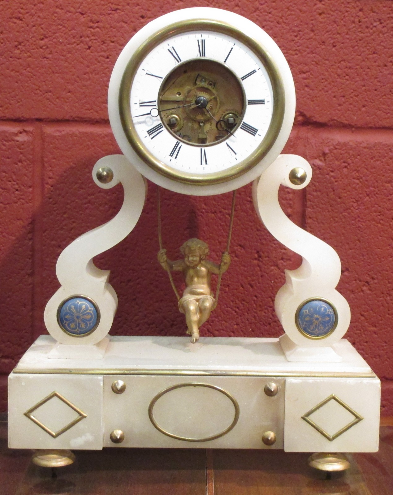 An alabaster mantle clock with swinging cherub pendulum