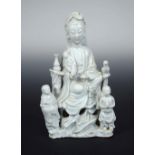 An 18th century blanc de Chine group of Guanyin, she sits on a rock with a vase to her right and a