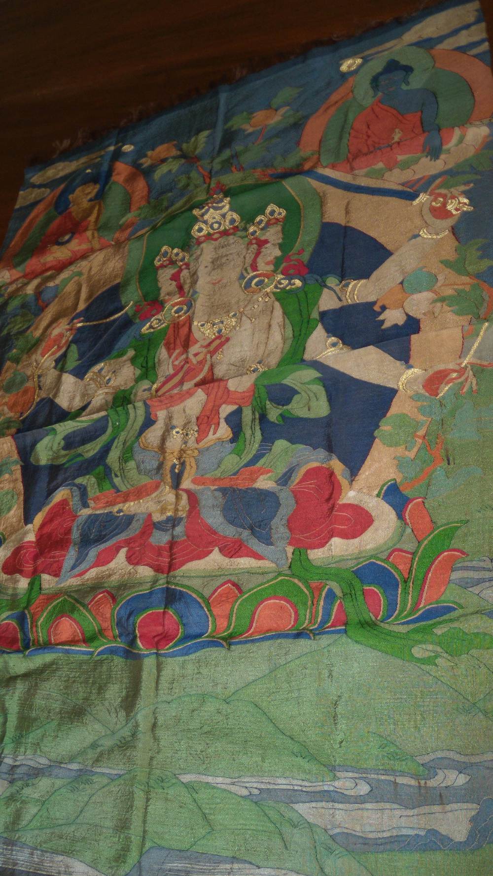 A Tibetan sewn silkwork thangka depicting a three headed deity with a bow, sword, pen and book in