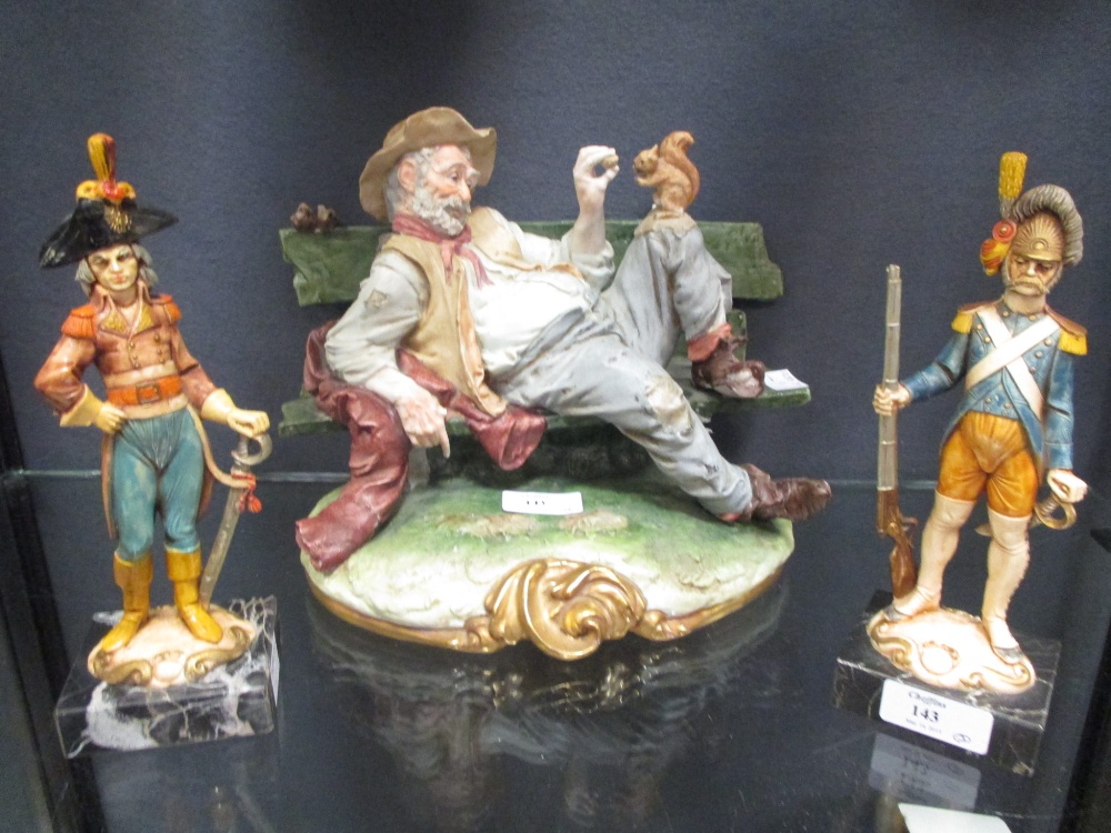 A Capidemonte style figure sitting on a bench and two model soldiers