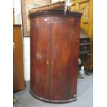 A George III mahogany bow fronted wall hanging corner cupboard