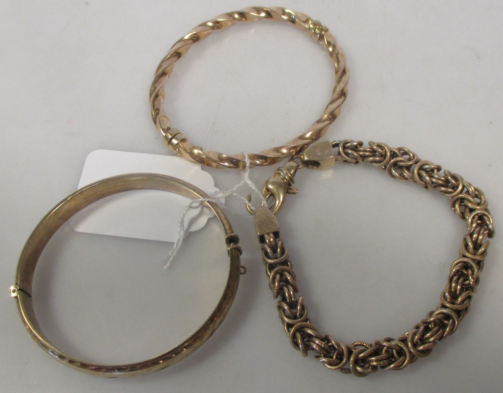 A 9ct gold bright cut engraved hinged bangle, a 9ct gold twisted hinged banlge and a 9ct gold