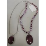 A collet mounted ruby cabochon pendant on a silver chain, together with another similar on a