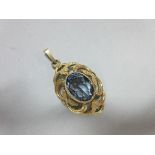 A synthetic light blue spinel pendant, the oval cut spinel collet set to a pierced scrolling and