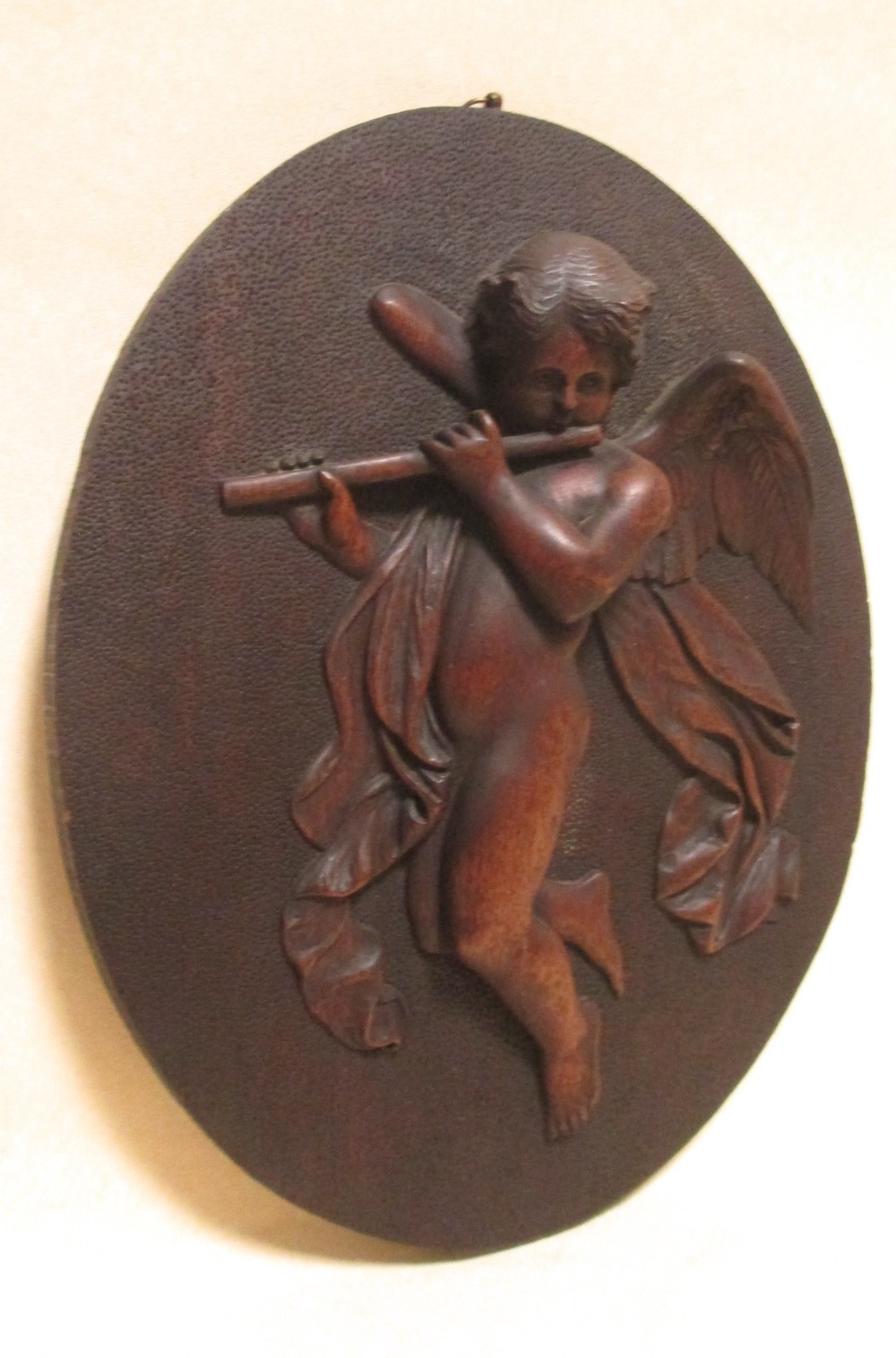 An oval relief panel of carved wood depicting a cherub flautist, 44 x 34cm