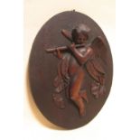 An oval relief panel of carved wood depicting a cherub flautist, 44 x 34cm