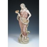 A Royal Dux figure of a Classical lady, she stands draped in a pink robe, a basket of crustacea in