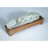 An 18th/19th century nephrite jade belt hook with later wood stand, the pale grey green stone of