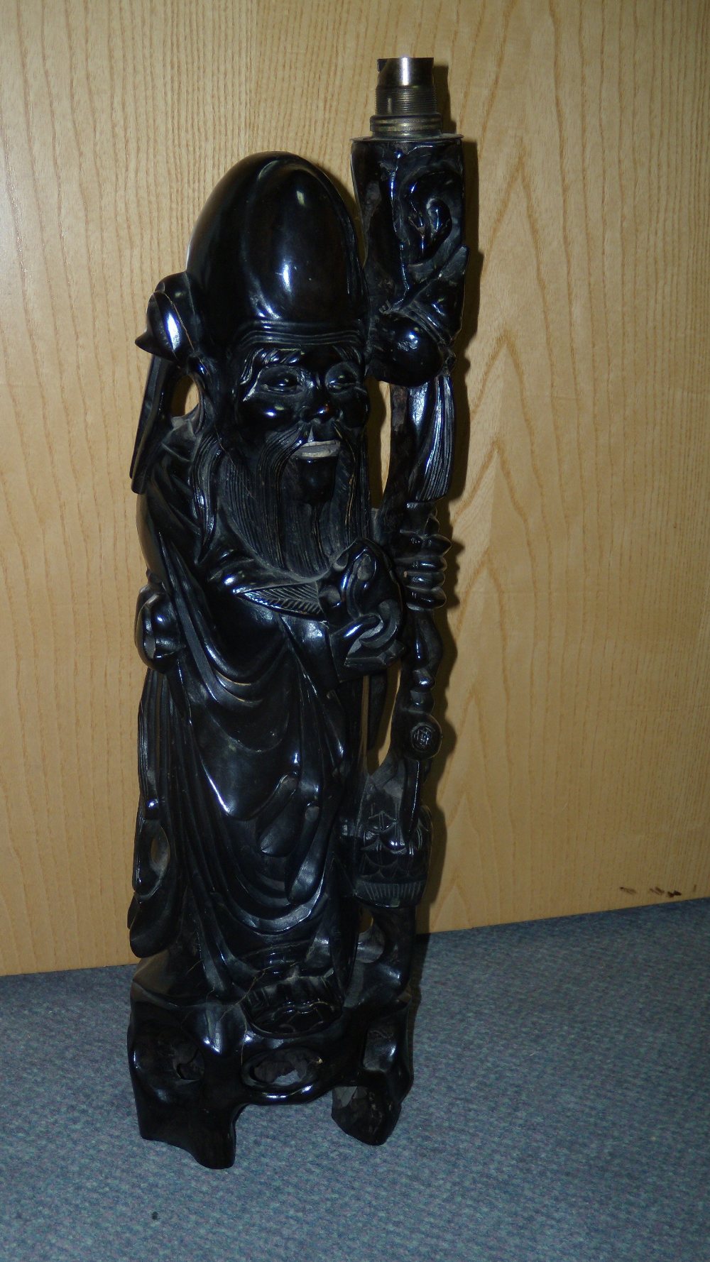 A hardwood carving of Shoulao as a lamp, he stands on a tripod base holding a peach in his right