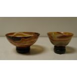 Two agate bowls on spinach green stone stands, the mottled brown and grey sides of the larger carved